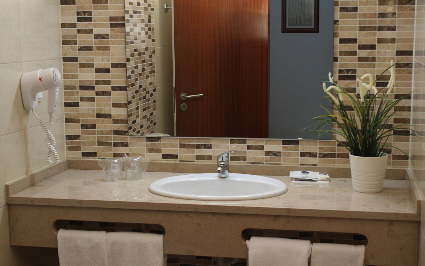 Waschbecken im Hotelbad mit Spiegel, Föhn und Pflanze