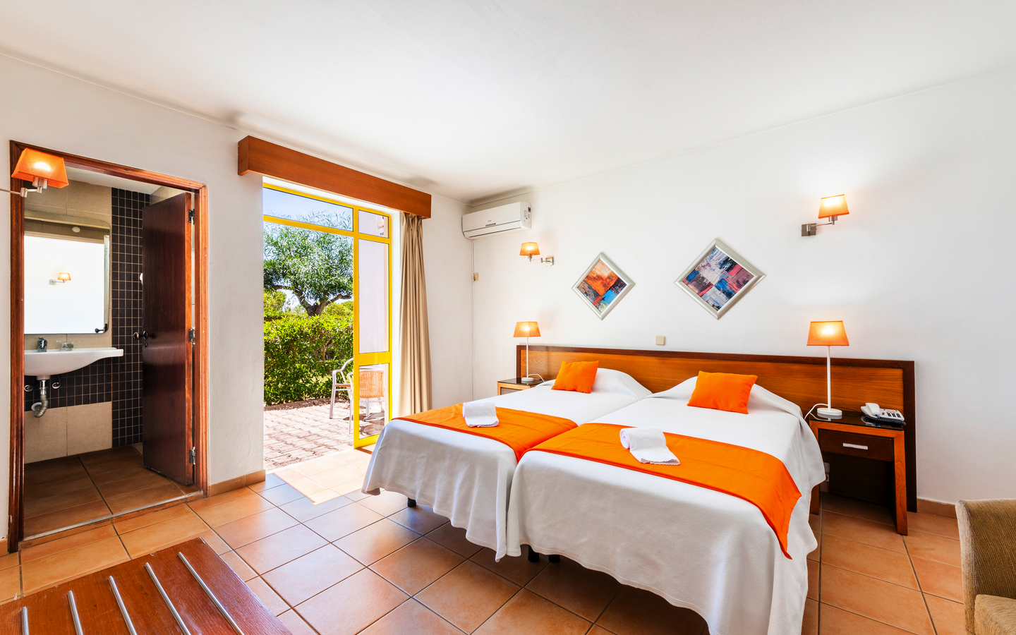 Helles Hotelzimmer mit zwei Betten, Balkon und angrenzendem Bad.