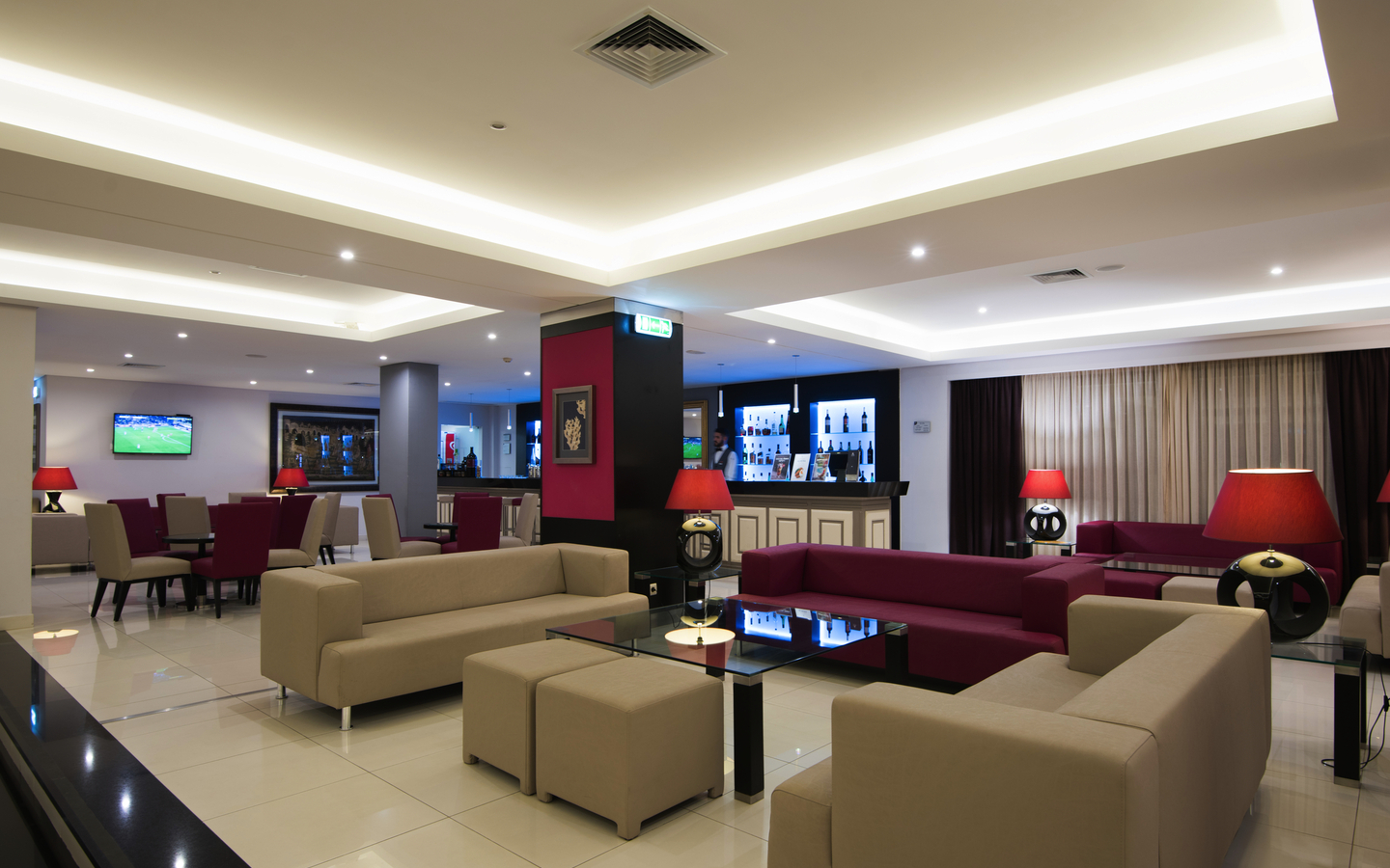Hotelbar mit modernen Sofas, Tischen und roten Akzenten in elegantem Ambiente.