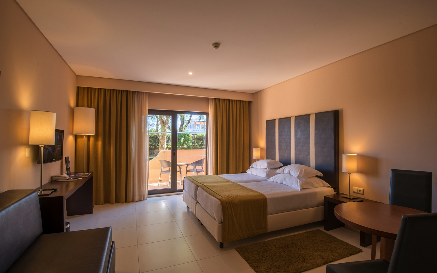 Modernes Hotelzimmer mit Doppelbett, Tisch, Stühlen und Balkon im Hintergrund.