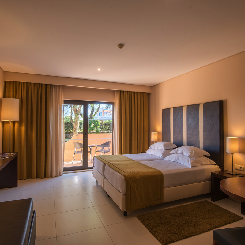 Modernes Hotelzimmer mit Doppelbett, Tisch, Stühlen und Balkon im Hintergrund.