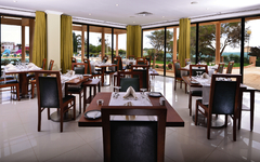 Helles Restaurant mit gedeckten Tischen und großen Fenstern, die in einen Garten blicken.