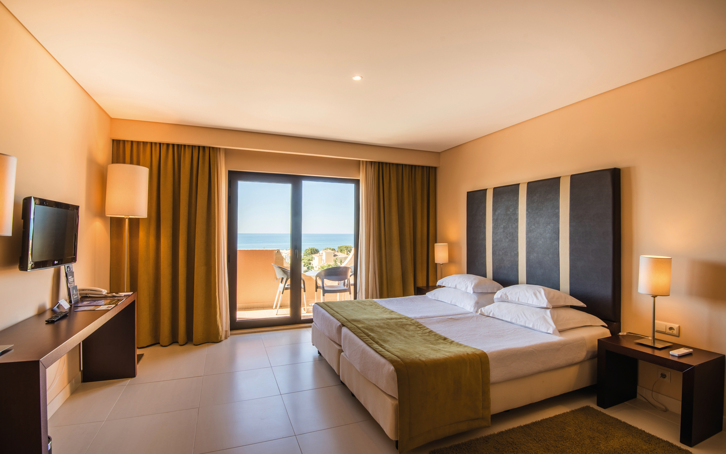 Helles Hotelzimmer mit Doppelbett und Balkonblick auf das Meer.