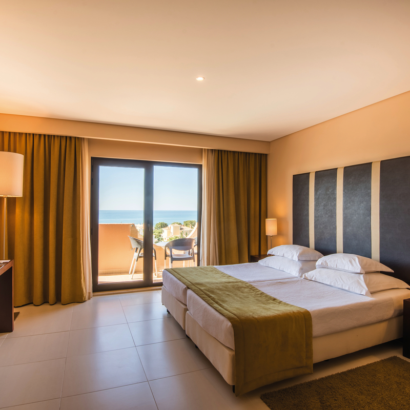 Helles Hotelzimmer mit Doppelbett und Balkonblick auf das Meer.