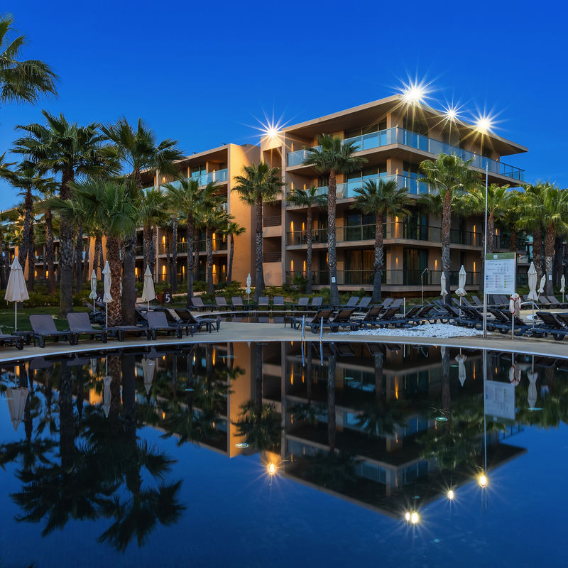 Hotel am Pool mit Liegestühlen, umgeben von Palmen bei Abenddämmerung.