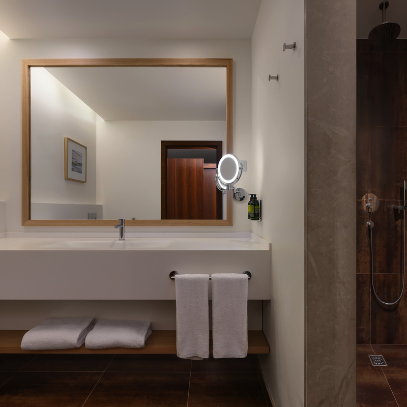 Modernes Hotelbad mit großem Spiegel, Waschbecken und offener Dusche.