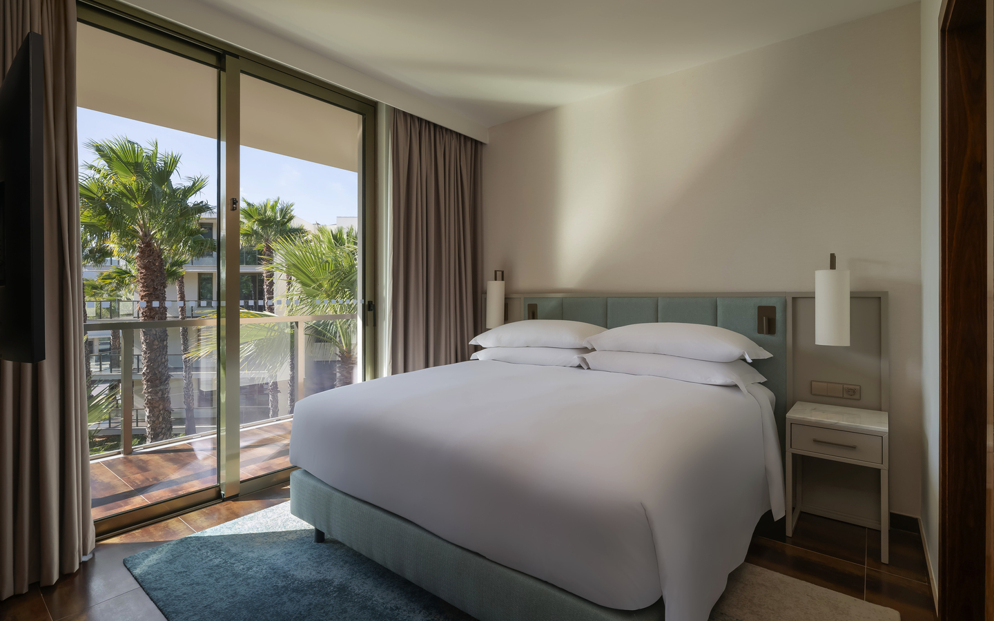 Helles Hotelzimmer mit Doppelbett, großer Fensterfront und Blick ins Grüne.