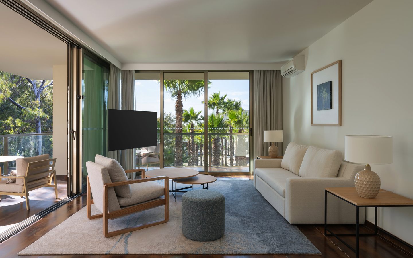 Helles Wohnzimmer mit modernen Möbeln und Blick auf Palmen durch große Fenster.