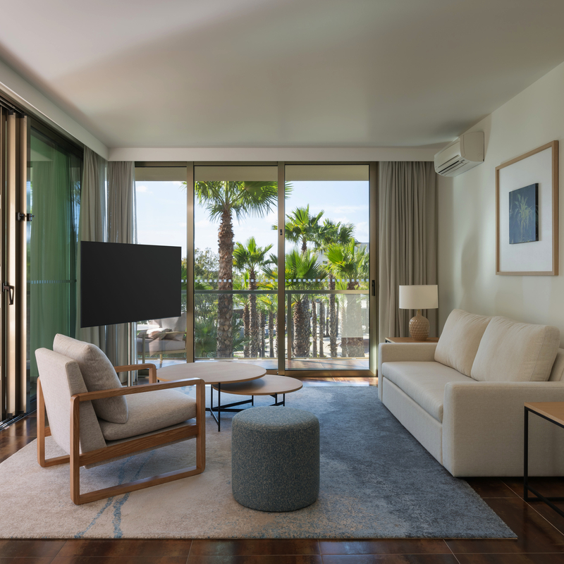 Helles Wohnzimmer mit modernen Möbeln und Blick auf Palmen durch große Fenster.