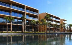 Hotelgebäude mit Palmen am Pool, blauer Himmel im Hintergrund.
