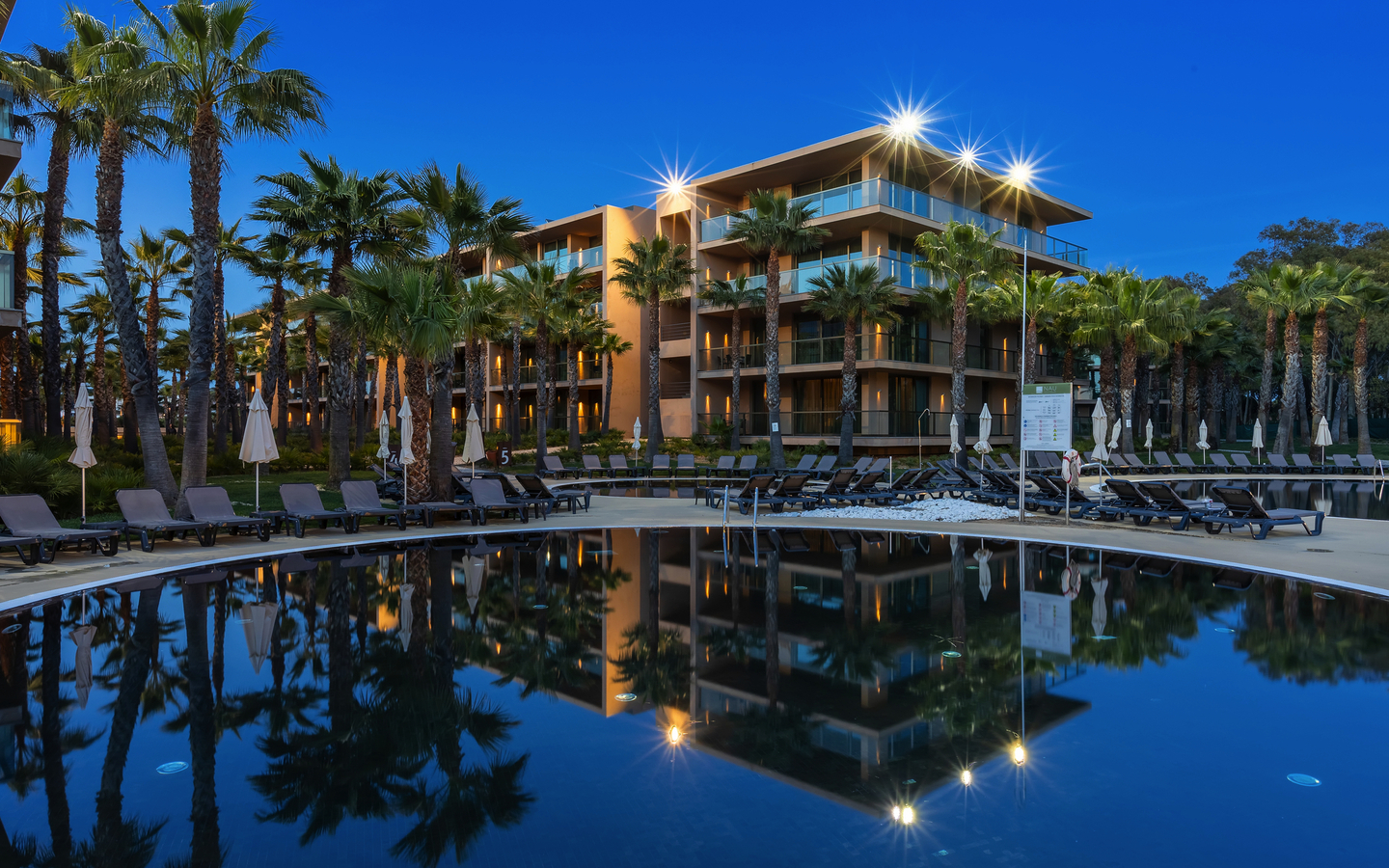 Hotel am Pool mit Liegestühlen, umgeben von Palmen bei Abenddämmerung.