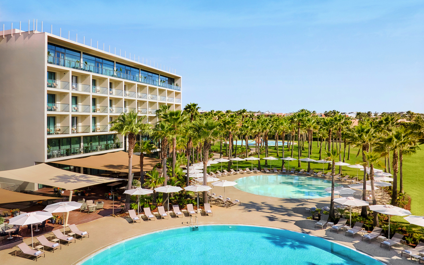 Hotel mit Palmengarten, Pool und Sonnenschirmen in Algarve, Portugal.