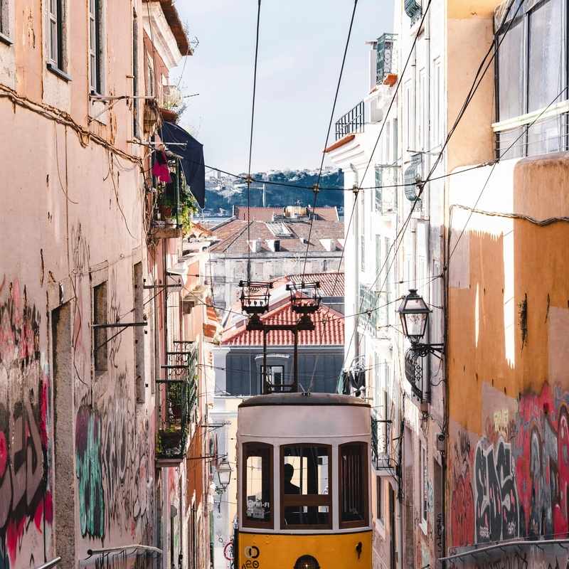 Gelbe Straßenbahn fährt eine steile, mit Graffiti versehene Straße hinauf.