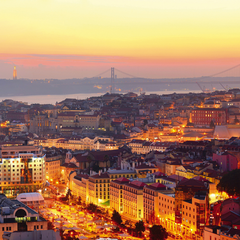 Städtische Skyline bei Sonnenuntergang, beleuchtete Gebäude und Brücke im Hintergrund.