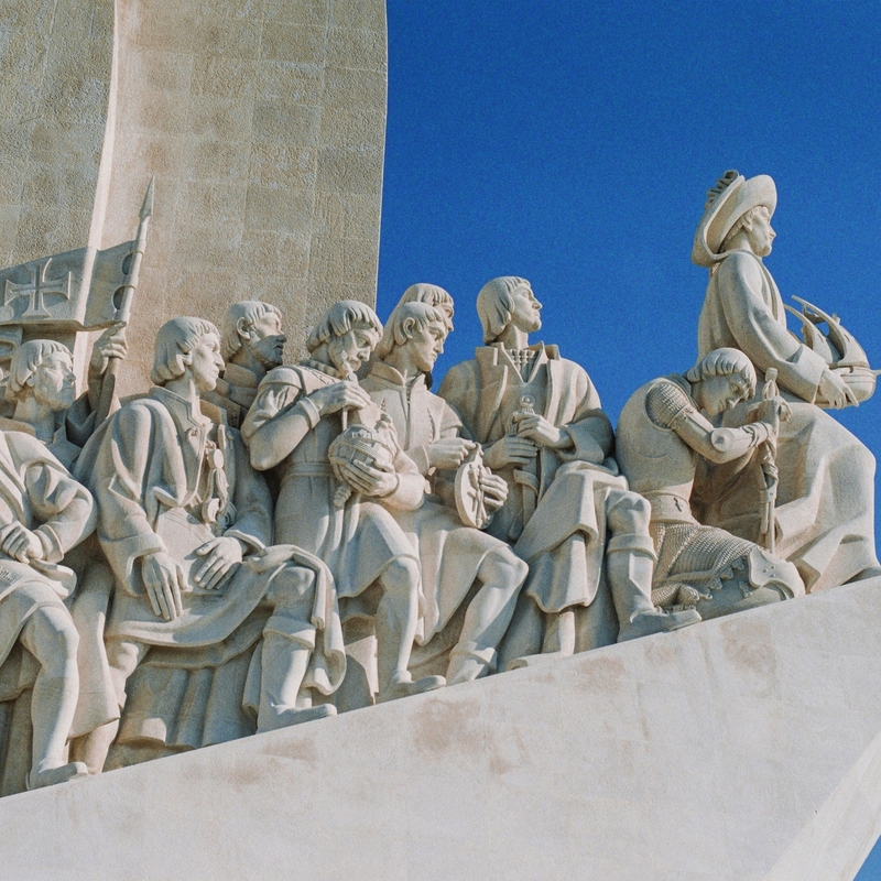 Statue von Entdeckern in einem Boot vor blauem Himmel.