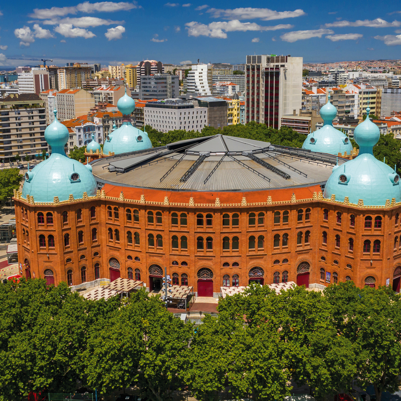 Luftaufnahme einer historischen Stierkampfarena in einer Stadt mit blauen Kuppeln.