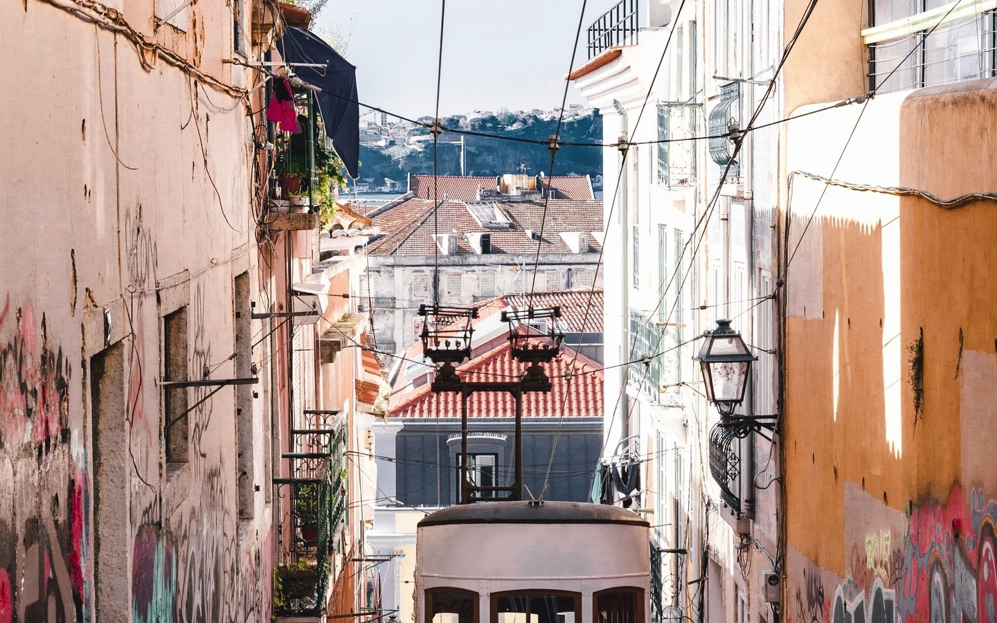 Gelbe Straßenbahn fährt eine steile, mit Graffiti versehene Straße hinauf.