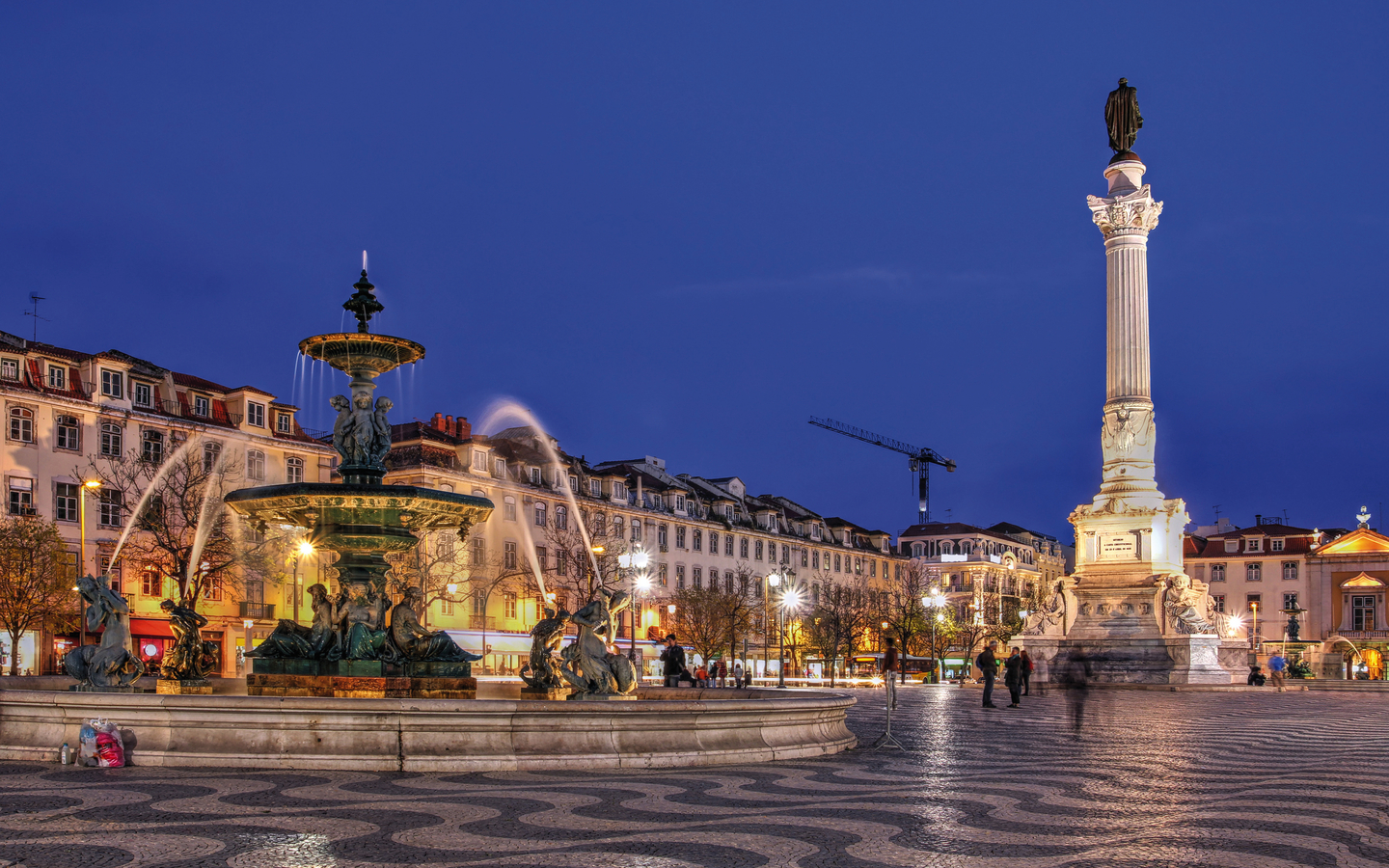 Springbrunnen und Statue auf einem Platz bei Nacht in einer europäischen Stadt.
