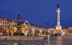 Springbrunnen und Statue auf einem Platz bei Nacht in einer europäischen Stadt.