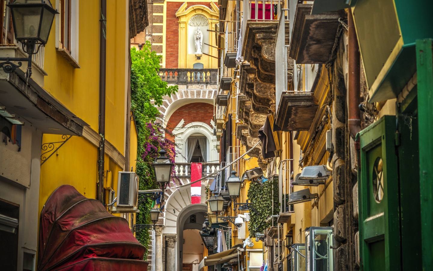 Schmale, belebte Gasse mit gelben Gebäuden und Balkonen in einer historischen Stadt.
