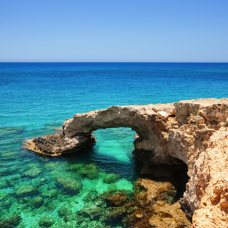 Steinbogen an der Küste mit klarem türkisfarbenem Meer und blauem Himmel im Hintergrund