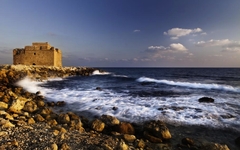Steinige Küste Zyperns mit altem Gebäude am Meer unter blauem Himmel.