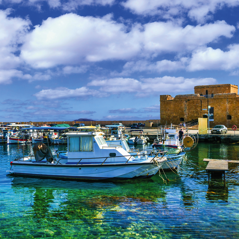 Hafen mit Booten vor Paphos Schloss auf Zypern bei blauem Himmel.