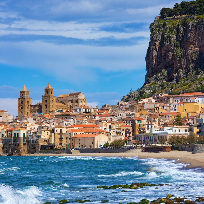 Küstenstadt mit historischer Architektur und Meer im Vordergrund.