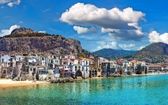 Küstenstadt mit Bergen und klarem Wasser, blauer Himmel mit Wolken im Hintergrund.