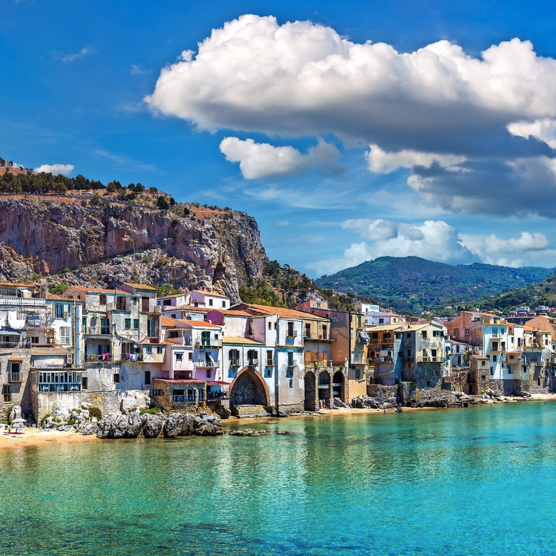 Küstenstadt mit Bergen und klarem Wasser, blauer Himmel mit Wolken im Hintergrund.