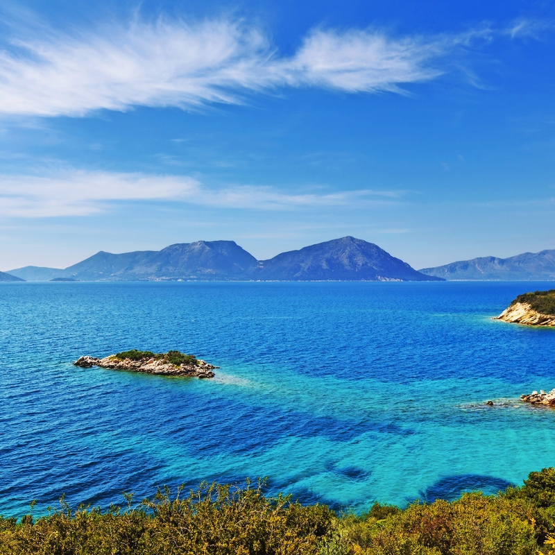 Blick auf blaues Meer mit Inseln und Bergen im Hintergrund bei klarem Himmel.