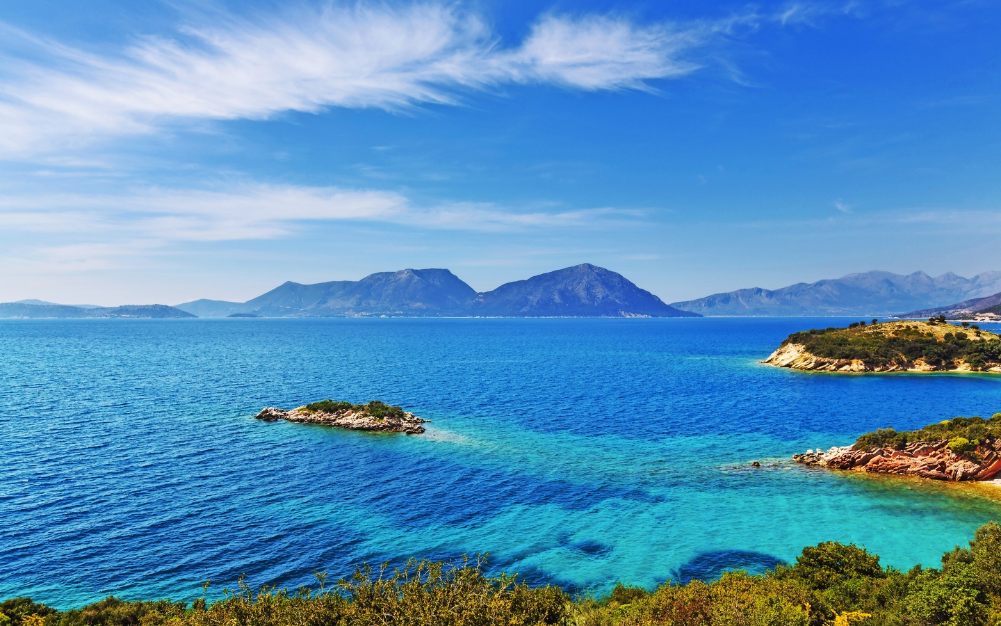 Blick auf blaues Meer mit Inseln und Bergen im Hintergrund bei klarem Himmel.
