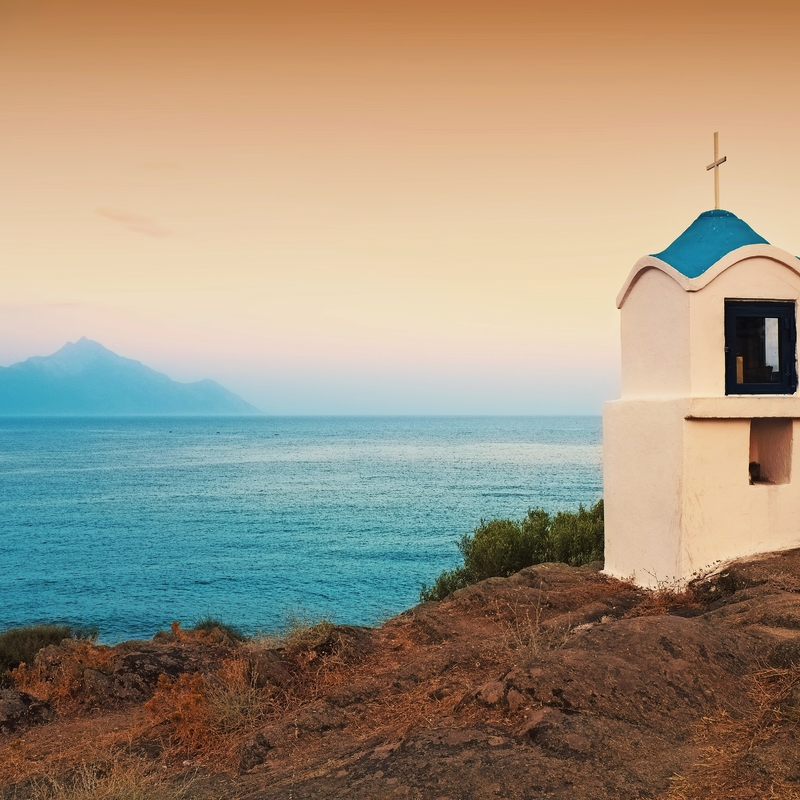 Weißes Gebäude mit blauem Dach am Meer bei Sonnenaufgang.