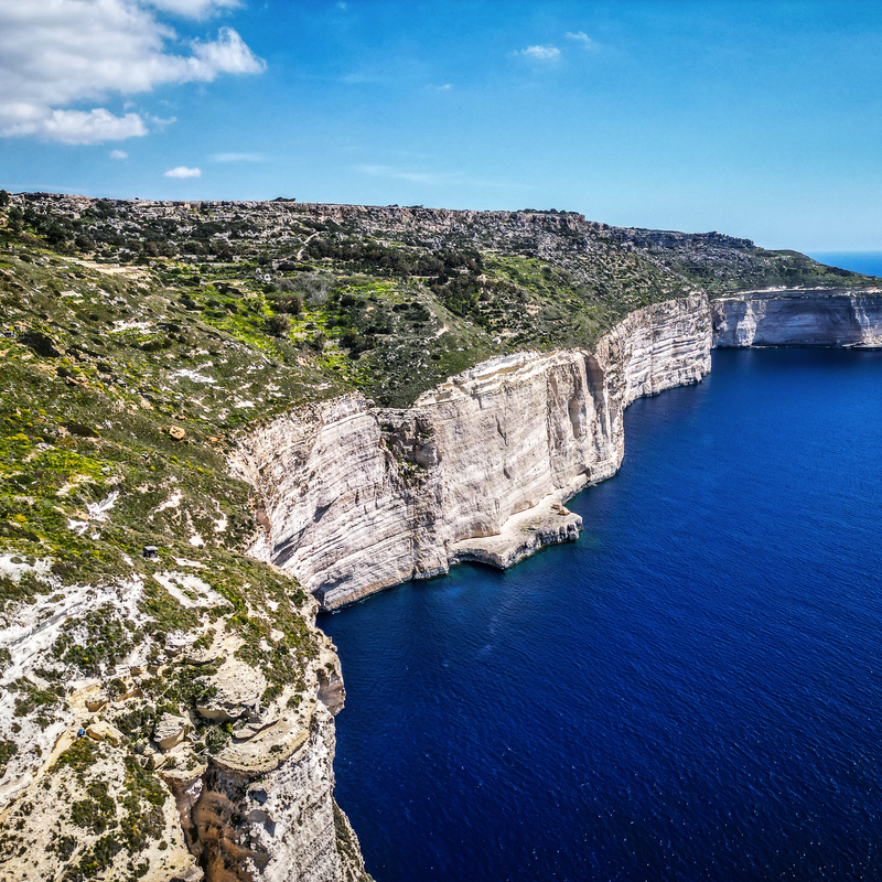 Klippen an einer Küste mit blauem Meer und grünem Land unter blauem Himmel.