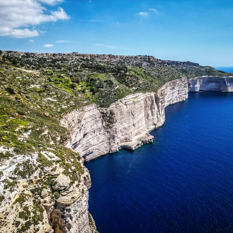 Klippen an einer Küste mit blauem Meer und grünem Land unter blauem Himmel.