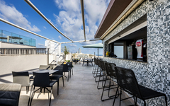 Dachterrasse eines Hotels mit Tischen und Stühlen unter blauem Himmel.