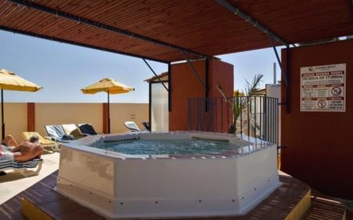 Ein Whirlpool auf einer Hotelterrasse mit Sonnenliegen und Sonnenschirmen.