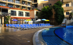 Außenpool mit blauen Liegestühlen und Sonnenschirmen am Hotelgebäude