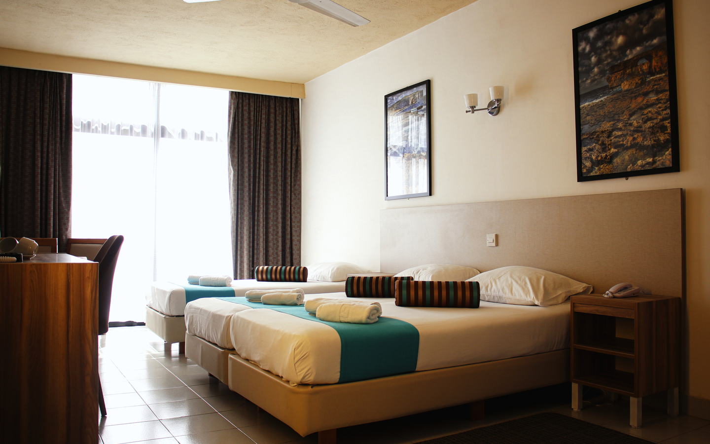 Hotelzimmer mit zwei Betten, einem Tisch und großen Fenstern.