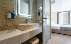Modernes Hotelzimmer mit Bad, Waschbecken und Bett im Hintergrund.