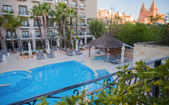 Hotelpool mit Sonnenliegen und Palmen in einem Resort in Malta.
