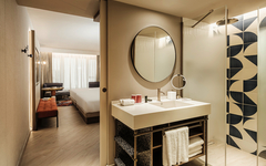 Modernes Hotelzimmer mit offenem Bad und einem runden Spiegel.