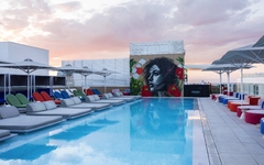 Pool auf Hotel-Dachterrasse mit Liegen und Wandgemälde bei Sonnenuntergang