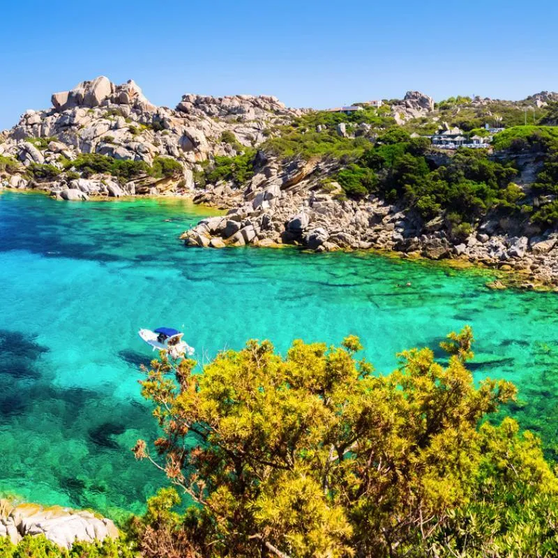 Bucht mit klarem türkisfarbenem Wasser, Felsen und grüner Vegetation.