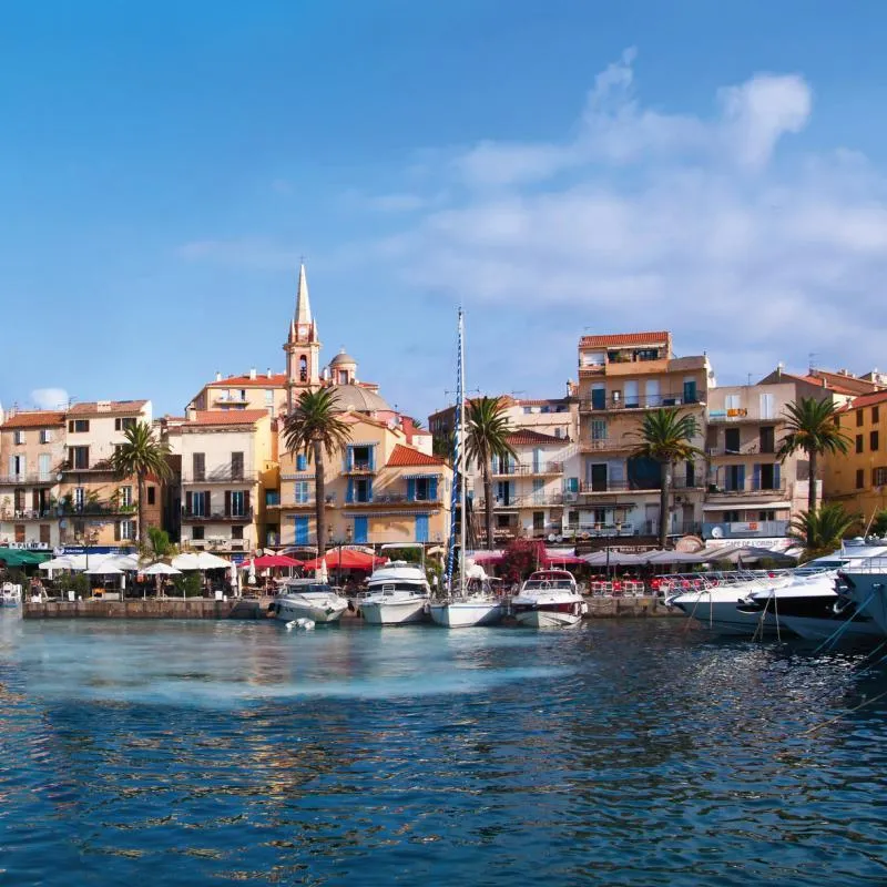 Hafen von Calvi auf Korsika mit Booten und pastellfarbenen Gebäuden im Hintergrund.