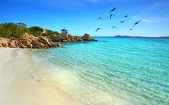 Strand mit klarem Wasser und Felsen an der Costa Smeralda, Sardinien, bei Sonnenschein.