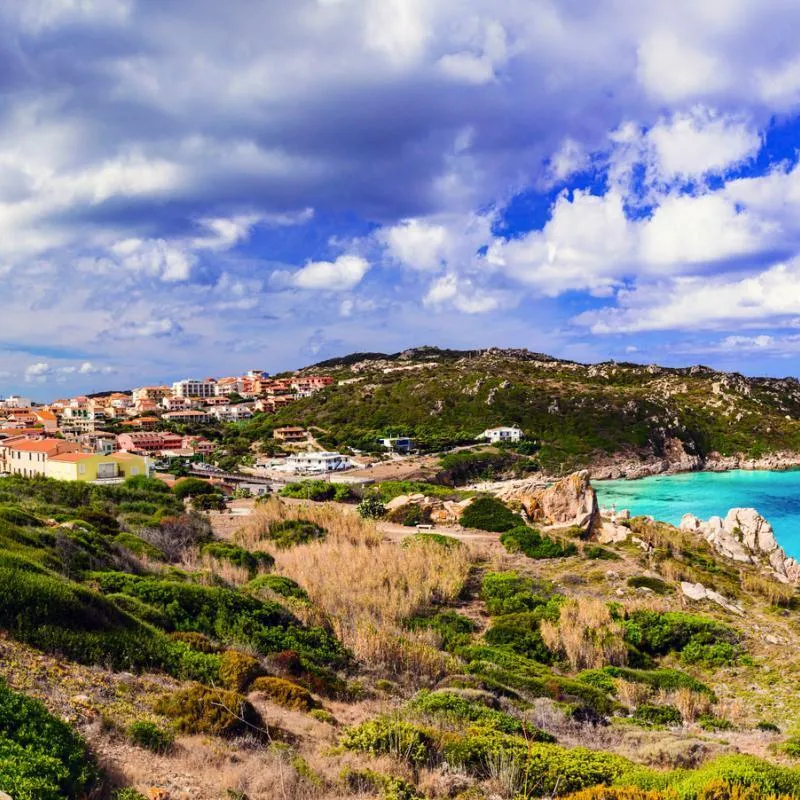 Küstenlandschaft mit Turm und Dorf auf Sardinien unter blauem Himmel.