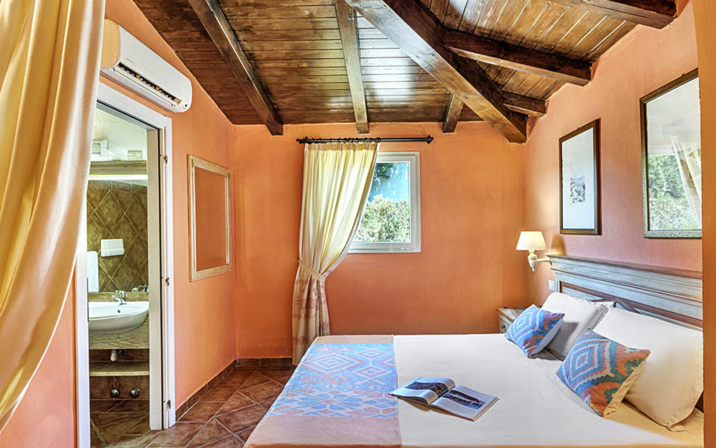 Helles Hotelzimmer mit Doppelbett, Holzbalkendecke und Bad im Hintergrund.