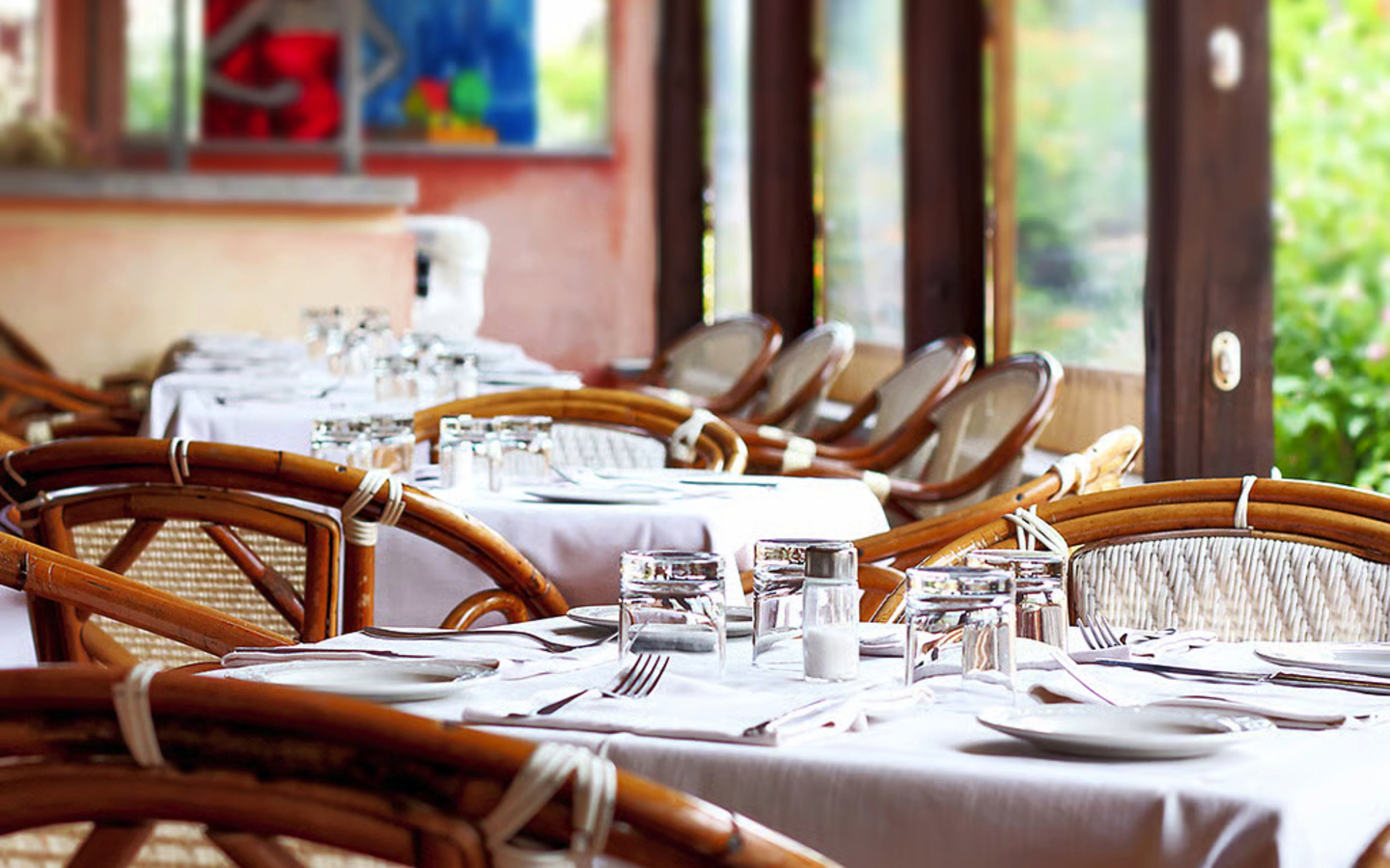 Restaurant mit gedeckten Tischen und Korbstühlen in einem offenen Raum.