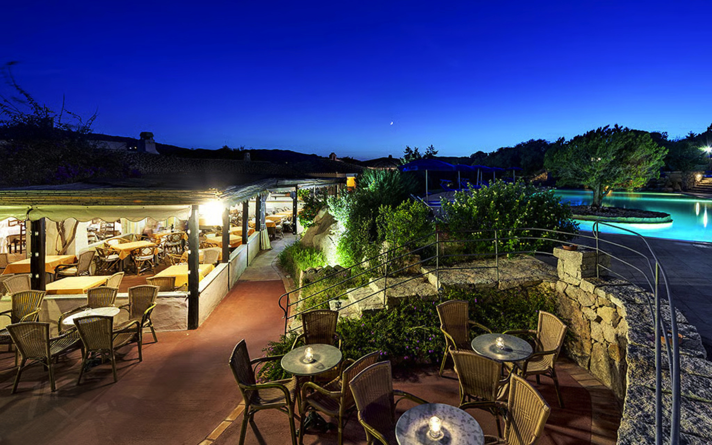 Terrasse eines Hotels in Sardinien bei Abenddämmerung mit Pool und Sitzbereich.
